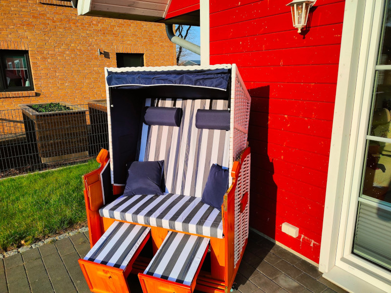 Blau-Weiß gestreift, gepolsterter, weißer Strandkorb auf der Terrasse in der Sonne.